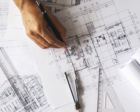 Persona revisando un plano arquitectónico sobre una mesa de trabajo con regla y lápiz